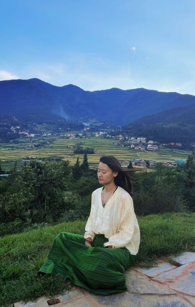 Yangchen seated in a Bhutanese mountain landscape